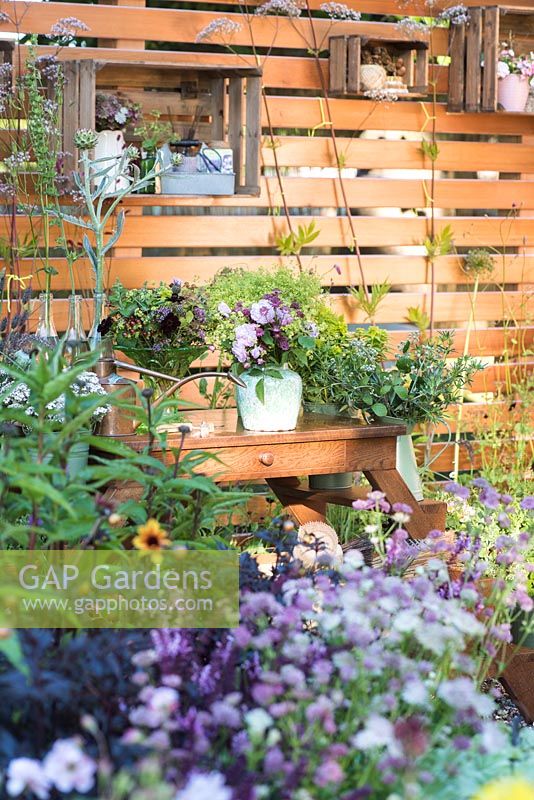 Wooden fence with shelves, work table with bouquets in pots and containers surrounded by summer flowers including Euphorbia schillingii and Valeriana officinalis. Katie's Lymphoedema Fund: Katie's Garden. Designers: Carolyn Dunster, Noemi Mercurelli, RHS Hampton Court Palace Flower Show 2016 