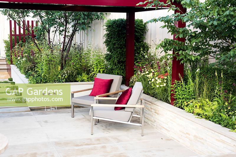 Relaxing and entertaining area with modern chairs next to raised flower bed in summer. Squire's 80th Anniversary Garden, Designer: Catherine MacDonald - Sponsor: Squire's Garden Centres 