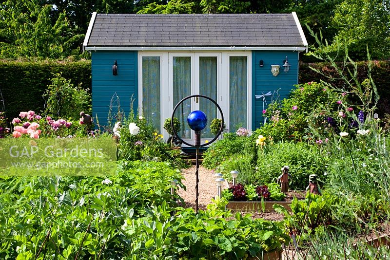 A summer-house in a vegetable garden planted with strawberries, potatoes, lettuce, broad beans and asparagus. A rusted bird sculpture in the centre