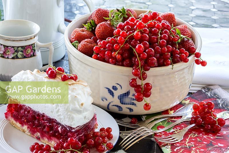 Redcurrants and strawberries in a bowl next to cake with meringue and silver cutlery