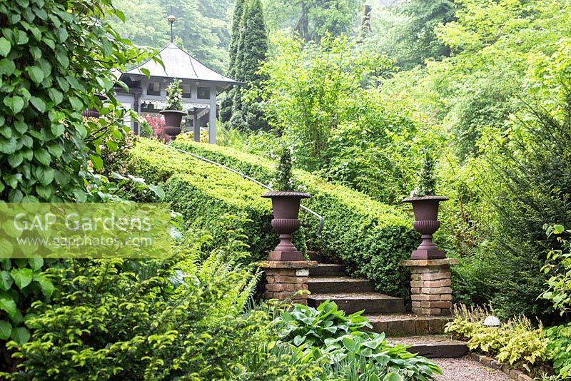 Antique metal vases on brick stone pillars to entrance of the garden stairway edged with box hedges