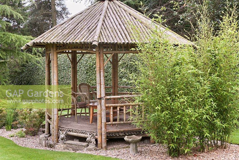 A bamboo gazebo with chairs set into gravel in an island bed.  Japanese style garden.  June, North Yorkshire. 