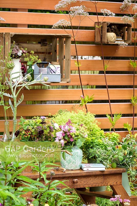 Vases with cut flowers placed on wooden crates used as shelves. Planting includes Alchemilla mollis, Rosa 'Blush Noisette', Eryngiums, Euphorbias, Astrantias, Sweet williams, Grasses and Seedheads. Katie's Lymphoedema Fund : Katie's Garden, RHS Hampton Court Palace Flower Show 2016