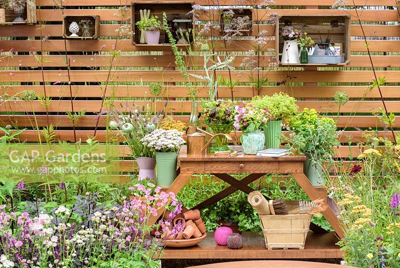 Wooden crates used as shelves and cut flowers in vases with Alchemilla mollis, Rosa 'Blush Noisette', eryngiums, euphorbias, astrantias, sweet williams, grasses and seedheads in Katie's Lymphoedema Fund: Katie's Garden, RHS Hampton Court Palace Flower Show 2016. Design: Noemi Mercurelli and Carolyn Dunster