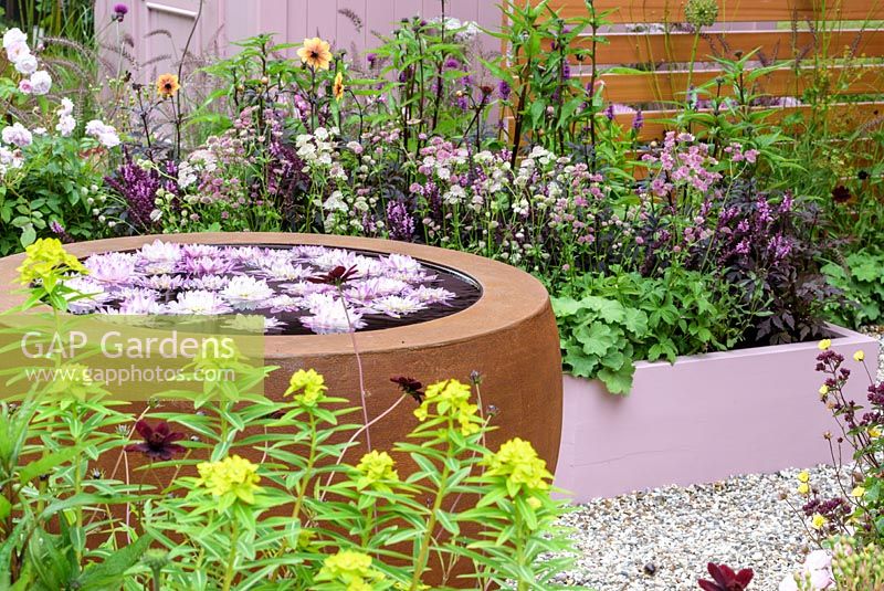 Urbis water feature in the centre, raised beds and crates on a slatted fence - Katie's Lymphoedema Fund: Katie's Garden, RHS Hampton Court Palace Flower Show 2016. Design: Noemi Mercurelli and Carolyn Dunster