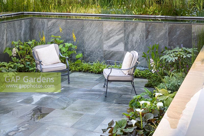 Sunken seating area with CED Natural stone Ebony Cloud Paving and two armchairs. Plants include Astilbe,'Sprite', Fatsia japonica 'Variegata, hostas and ligularia. Perennial Immerse Garden, RHS Hampton Court Flower Show 2016. Designed by Cherry Carmen