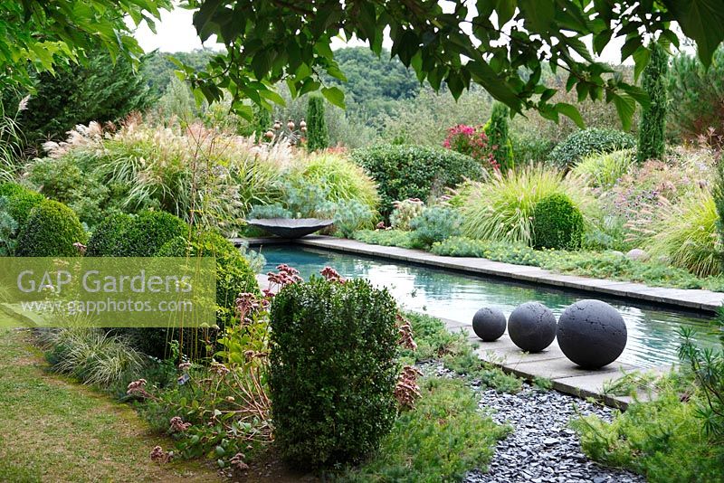 Three stoneware balls are placed by the side of the pool of the Contemporary Garden, Les Jardins de la Poterie Hillen