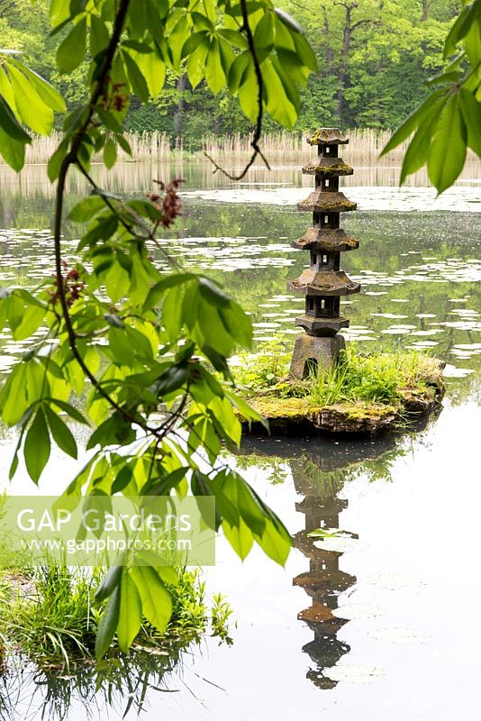 Oriental statue on its own tiny island, makes a focal point off the shoreline of the lake in the naturalistic Japanese area near the castle wall. Framed by Aesculus flava 'Vestita' - sweet buckeye, a member of the horse chestnut family.