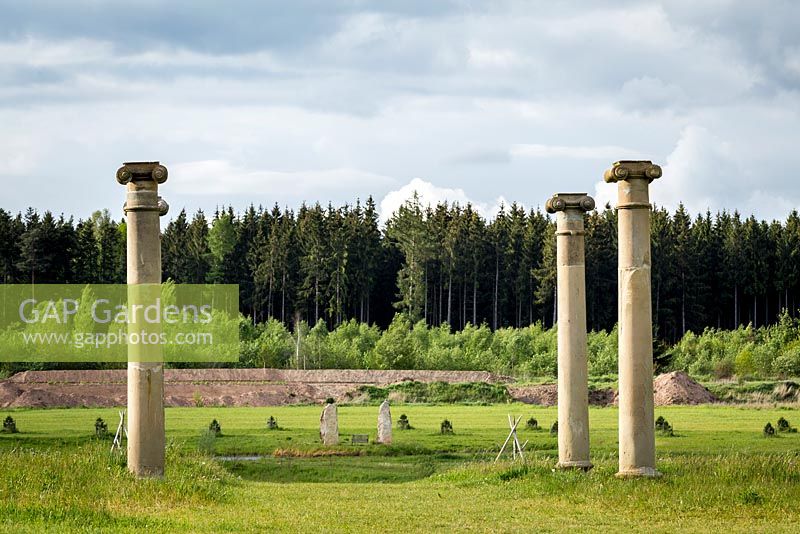 Ionic Columns in the classical Greek tradition stand in the Landscape Park with the neighbouring forest behind.
