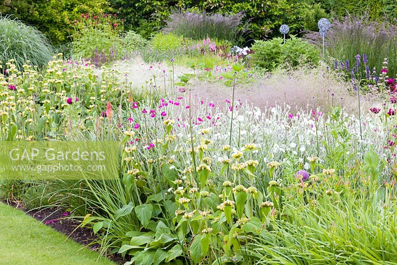 Contemporary metal ornaments rise above a large herbaceous border at Bluebell Cottage Gardens, Cheshire - photographed in June. Plants including: Phlomis russeliana, Lychnis coronaria, Agastache, Kniphofia and Stipa