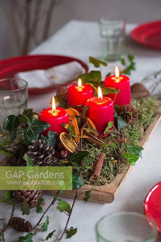 A festive centrepiece constructed from Moss, Pine cones, Cinnamon sticks, Ivy, dried Orange slices and lit candles