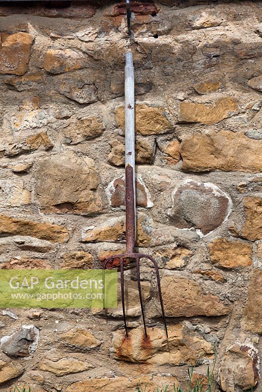 Old rusty garden fork hanging on stone wall 