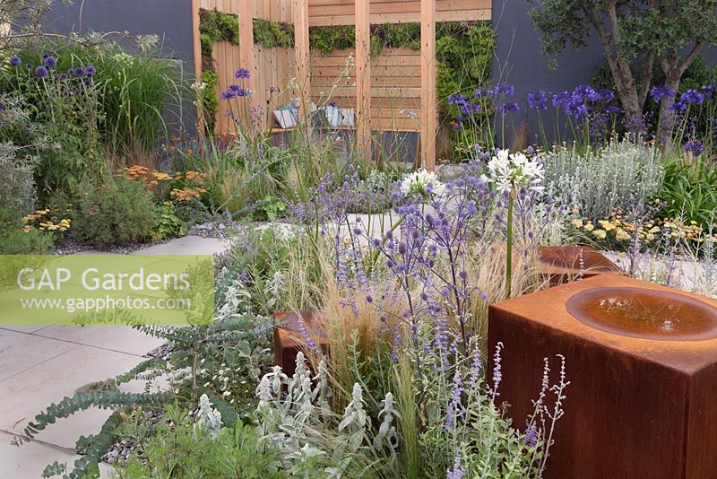 Rusty metal cubes amongst drought tolerant perennial planting and a wooden arbour seating area in patio garden - Coastal Retreat at RHS Tatton Park Flower Show 2016