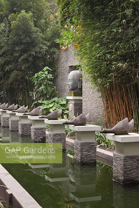 A formal rectangular pond with geese sculptures on stacked slate plinths and a large Buddah head - Java, Indonesia
