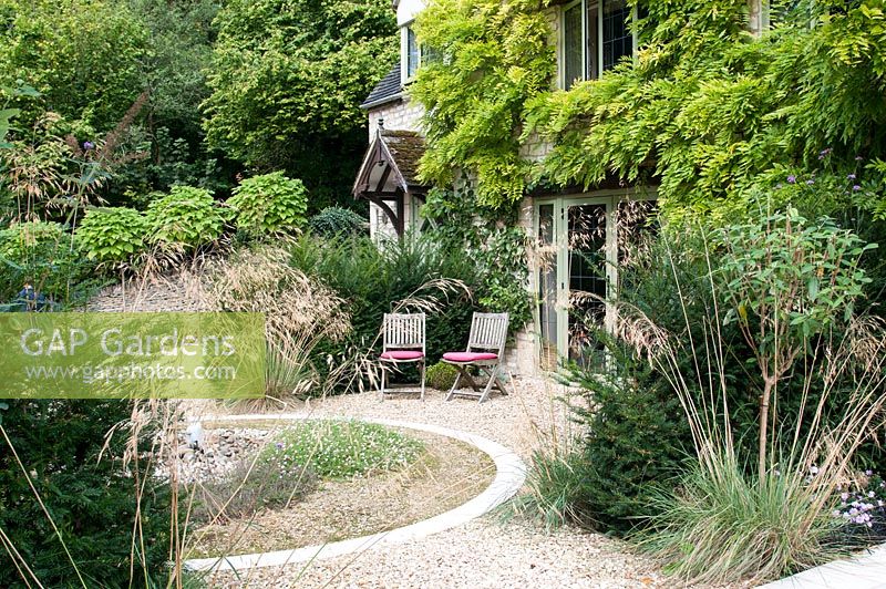 Seating area by house with gravelled circular water feature and planting of Stipa gigantea Taxus baccata Wisteria and Catalpa bignonioides 'Aurea' standards