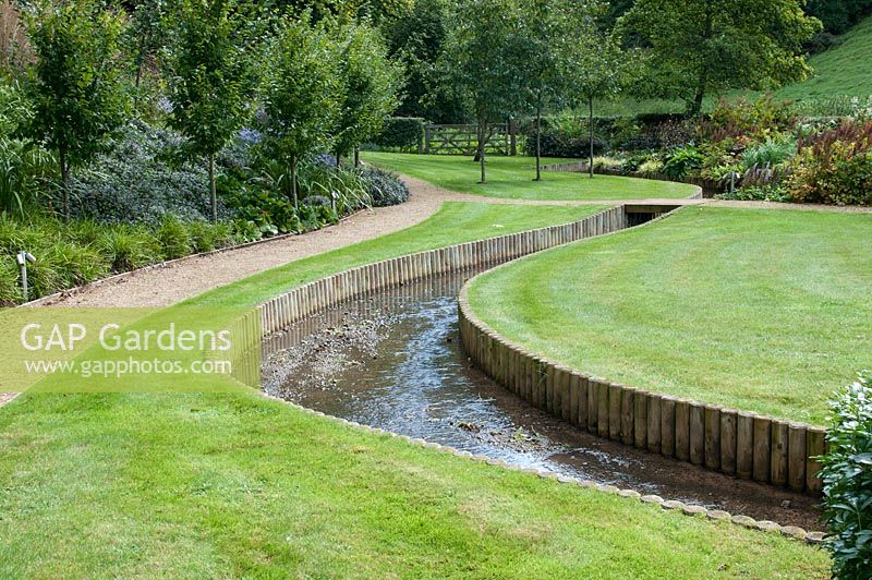 Curving gravel paths lawn and stream. Hawkley Cottage Gloucestershire September 