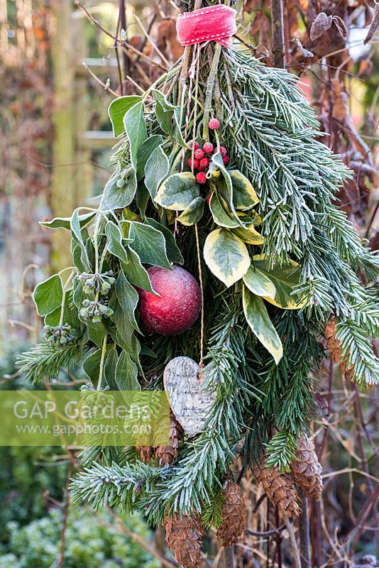 Frosty hanging bouquet of christmas foliage with bauble and heart in garden