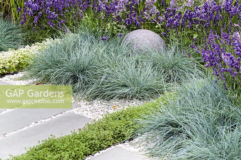 Stone globe and grey stone slabs surrounded by Festuca glauca, Lavandula angustifolia and  Thyme. Living Landscapes: Healing Urban Garden, RHS Hampton Court Palace Flower Show 2015. Designer Rae Wilkinson