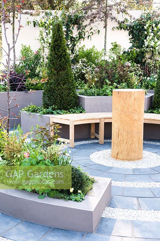 Macmillan Legacy Garden, View of the circular seating area with wooden benches, sculpture and raised concrete flowerbeds planted with Taxus Baccata Cone topiary, Hedera helix, Leucojum aestivum 'Gravetye Giant', Exochorda serratifolia 'Snow White', Viburnum tinus, Malus x moerlandsii 'Profusion'. Designer: Sarah Wilson, Sponsor: Macmillan Cancer Support , RHS Flower Show Cardiff 2017