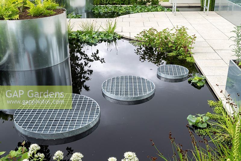 Contemporary water feature with metallic planters and grated steps across black water.
