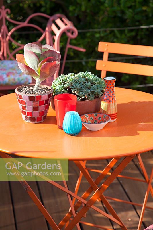 Decorative bright orange garden furniture with colourful ornaments and succulents in pots. Patio garden. Owner: Pattie Barron
