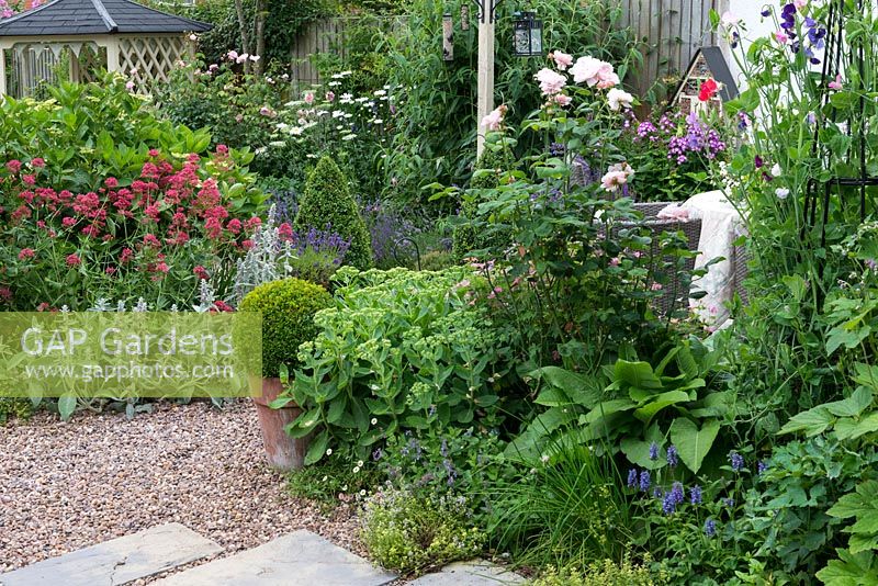A patio is sheltered behind obelisk of sweet peas, roses and herbaceous planting, with a pebble path linking to the side gate and gazebo.