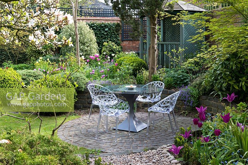 A circular patio enclosed by a raised bed. The table is made by Tom Faulkner and chairs by Lomos no. 8.