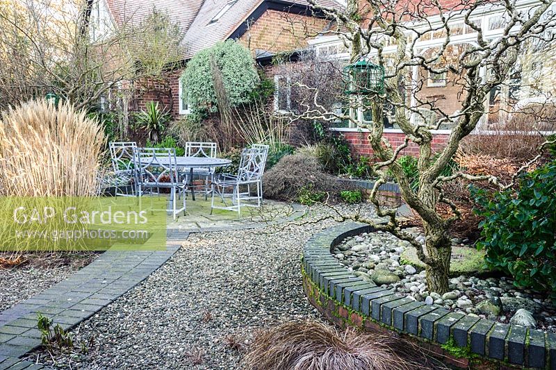 Seating area at the back of the house surrounded by planting including grasses such as Miscanthus sinensis 'Yakushima Dwarf' and a raised bed of shrubs in foreground. Windy Ridge, Little Wenlock, Shropshire, UK