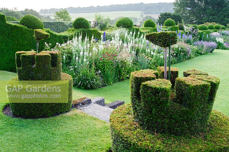 Topiary castles complete with flags overlook the herbaceous borders. Felley Priory, Underwood, Notts, UK