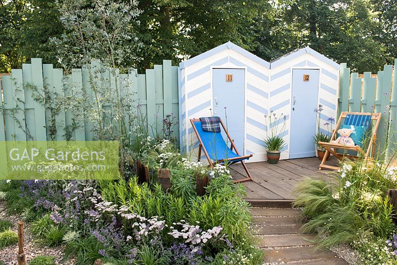 Blue and white painted beach huts with deck chairs on decking, Eucalyptus gunnii 'Azura' underplanted with Achillea millefolium 'Wonderful Wampee', Nepeta racemosa 'Walker's Low' - By The Sea, RHS Hampton Court Palace Flower Show 2017
