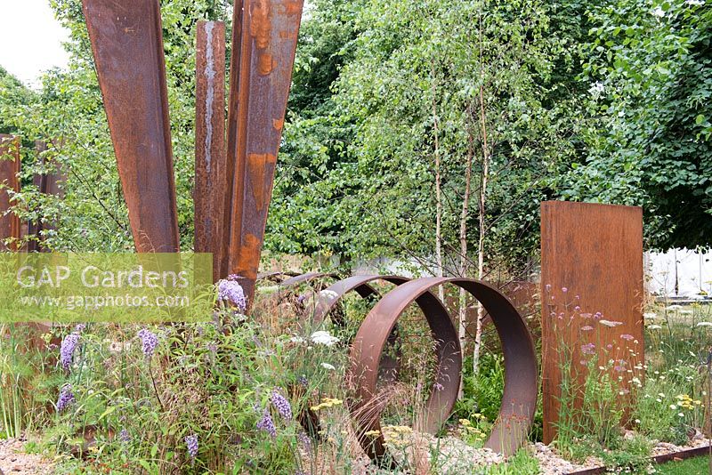 Self-seeded perennials surround rusted steel structures, including Buddleja davidii, Achillea 'Moonshine', Verbena bonariensis and Pilosella aurantiaca -  Brownfield Metamorphosis, RHS Hampton Court Palace Flower Show 2017