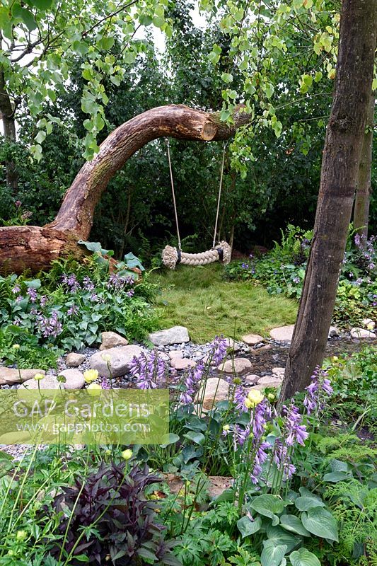 The Zoflora and Caudwell Children's Wild Garden. Garden swings on fallen tree trunk. Designers: Adam White and Andree Davies. Sponsors: Zoflora. RHS Hampton Court Palace Flower Show 2017
