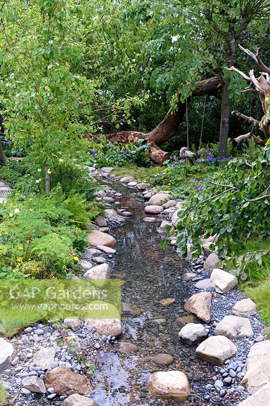 The Zoflora and Caudwell Children's Wild Garden. Shallow stream in woodland garden with edging of rocks and pebbles. Designers: Adam White and Andree Davies. Sponsors: Zoflora. RHS Hampton Court Palace Flower Show 2017