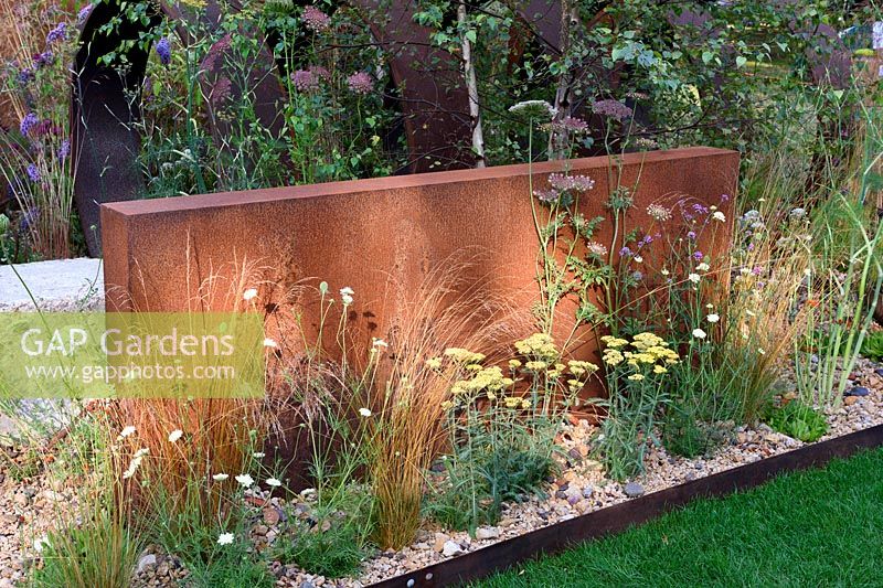 Brownfield - Metamorposis. Planting in gravel bed with the backing of large steel structure, Achillea and grasses, Design: Martyn Wilson. Sponsors: St. Modwen. RHS Hampton Court Palace Flower Show 2017