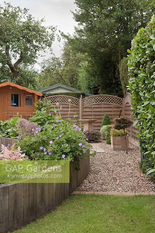 Corner of garden with upright railway sleepers creating raised beds next to evergreen hedge and fence - June, Summerfield Place, Cheshire