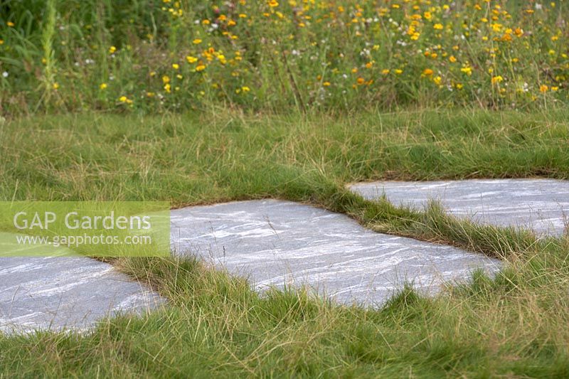 The Zoflora and Caudwell Children's Wild Garden. Pathway of smooth slabs between long grass, bordered with wild flowers. Designers: Adam White and Andree Davies.  Sponsor: Zoflora.