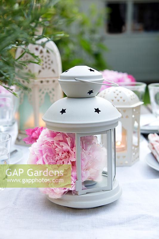 Table decorated with an eclectic mix of white lanterns and peonies, with peonies inside one of the lanterns