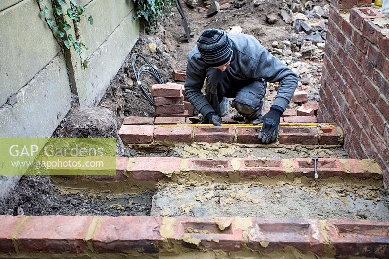Builder laying bricks to make steps in a small London Garden
