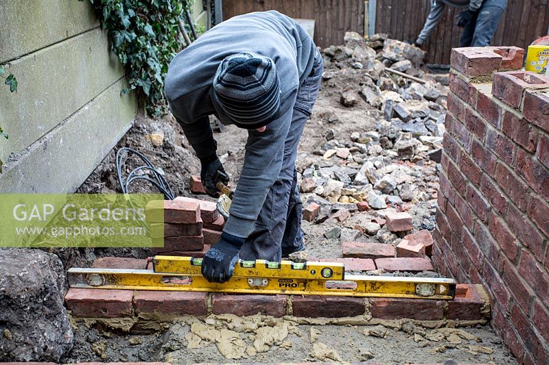 Builder laying using spirit level to square bricks for steps in a small London Garden