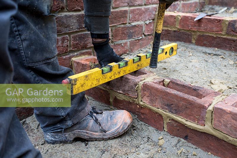 Builder laying using spirit level to square bricks for steps in a small London Garden