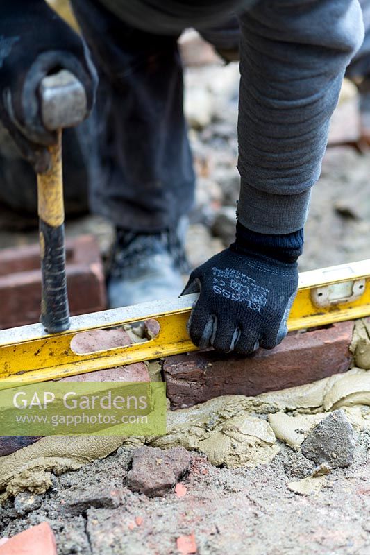 Builder using spirit level to square bricks for steps in a small London Garden