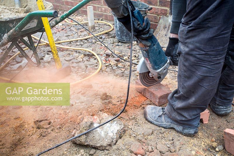 Builder using angle grinder to cut bricks for make steps in a small London Garden