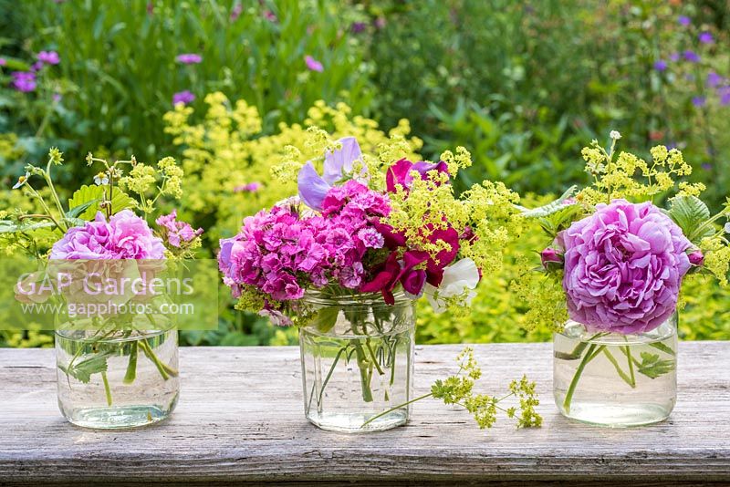 Summer floral arrangement in glass jars with roses, alchemilla mollis, Dianthus barbartus, sweet peas and fragaria barbartus