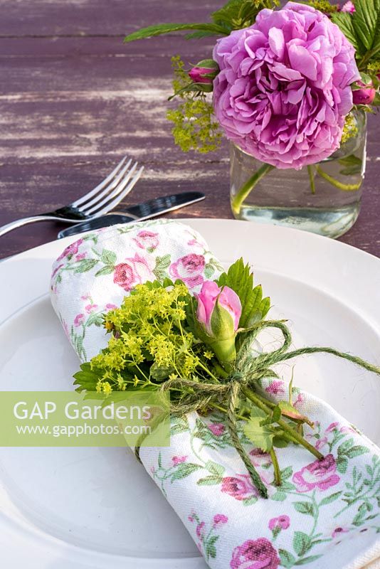 Summer table place setting with pink roses, alpine strawberry flowers and alchemilla mollis