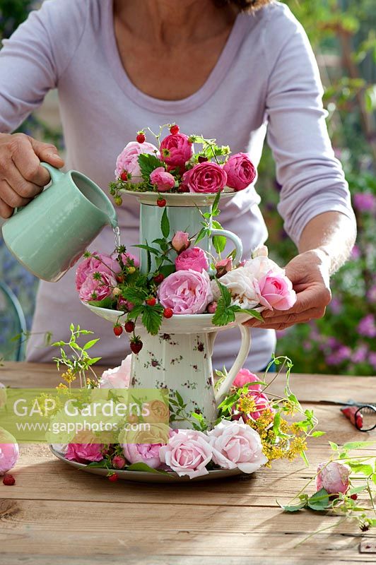 Woman arranging flowers on tiered stand made from jugs and plates