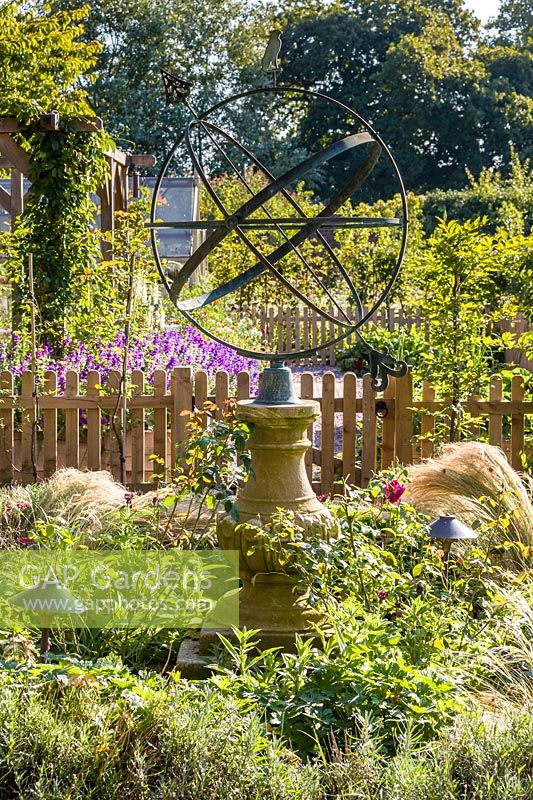 An armillary sphere provides a focal point in a modern Cheshire country garden, designed by Louise Harrison-Holland. Planting includes roses and Stipa tenuissima.