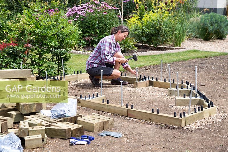 Woman hammering metal stakes into bottom of raised bed to secure into the ground