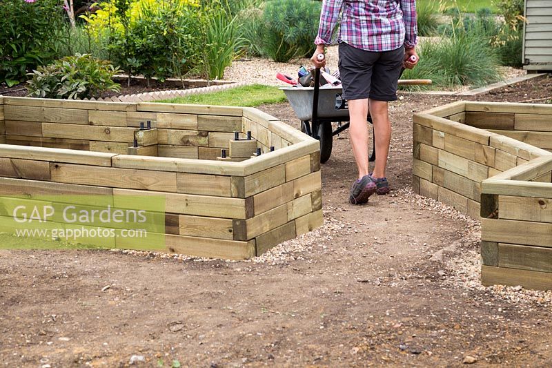 Woman walking away from home constructed wooden raised bed with her tools