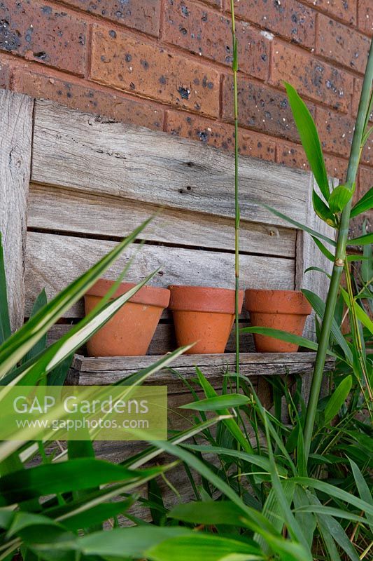 A recycled timber shelf display mounted to a brick wall with three decorative terracotta pots.