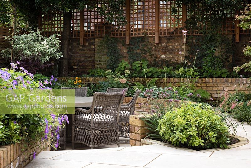 Late Summer garden with seating area and raised beds with Geranium 'Rozanne' and Choisya 'Aztec Pearl'